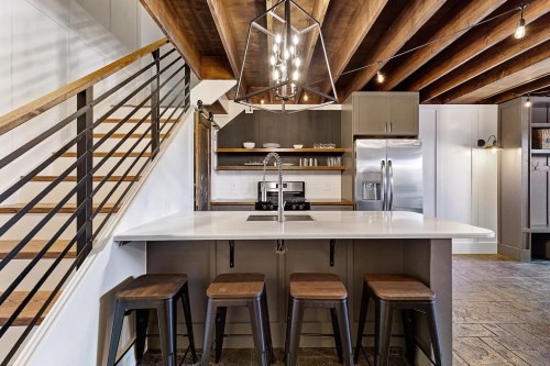 Modern kitchen with a large island, bar stools, stainless steel appliances, and wooden beams overhead.