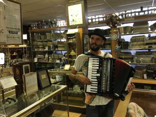 A man in a hat plays an accordion in a museum filled with musical instruments and artifacts.