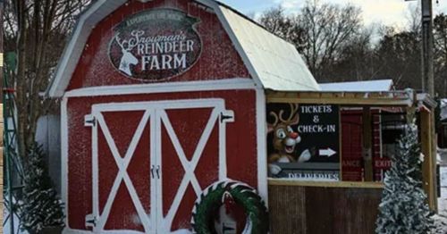 A festive red barn with a sign for a reindeer farm, surrounded by snow and holiday decorations.