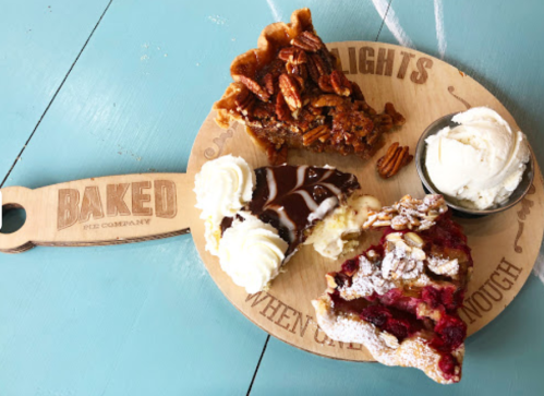 A wooden platter with four slices of pie: pecan, chocolate, and fruit, accompanied by a scoop of ice cream.