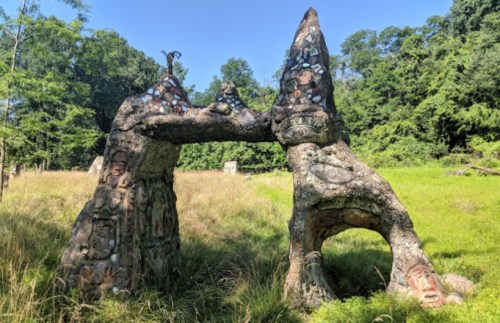 A unique stone sculpture resembling two figures, adorned with faces and patterns, set in a grassy landscape.