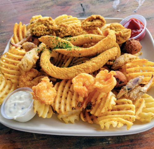A plate of crispy waffle fries topped with fried chicken, shrimp, and dipping sauces.