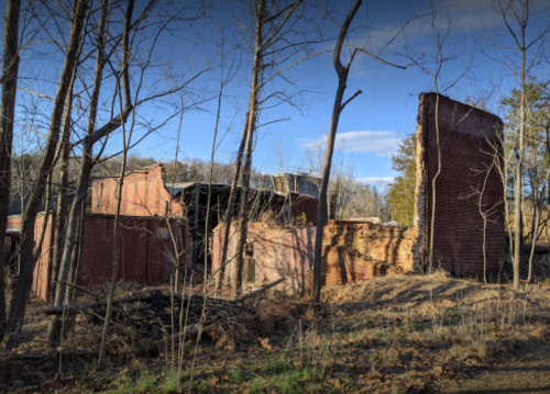 Abandoned brick ruins surrounded by trees and underbrush, with a clear blue sky in the background.