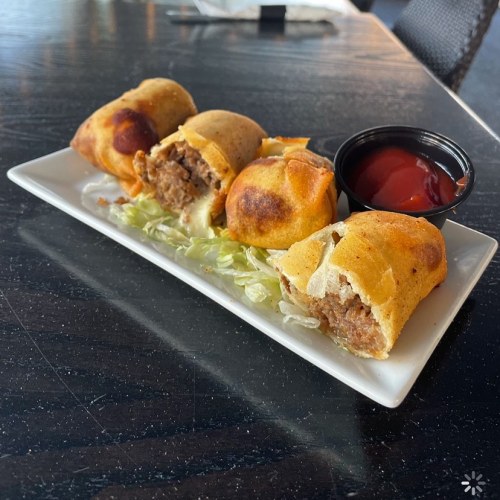 A plate of golden-brown egg rolls filled with meat, served with a side of ketchup and lettuce.