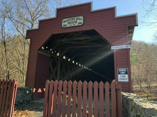 A red covered bridge with a sign reading "Martin's Mill Bridge," surrounded by trees and a wooden fence.