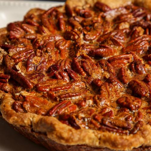A close-up of a golden-brown pecan pie topped with shiny, toasted pecans.