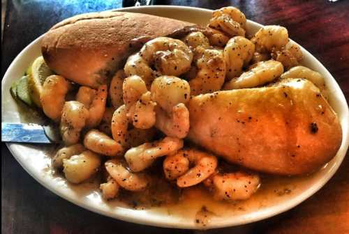 A plate of shrimp in sauce, served with two bread rolls and lemon slices.