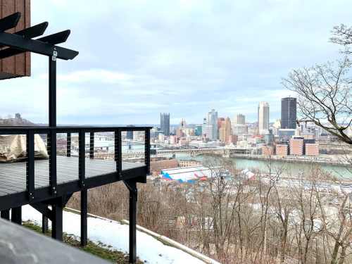 View of Pittsburgh skyline from a balcony, featuring buildings, a river, and trees in the foreground.