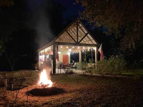 A cozy cabin at night with a campfire in front, surrounded by trees and illuminated by string lights.