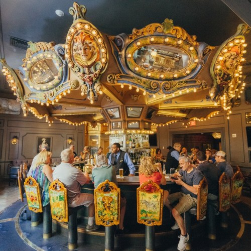 A vibrant bar with ornate decor and mirrors, featuring patrons enjoying drinks at a circular counter.