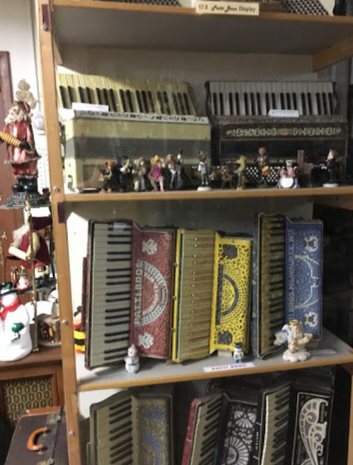A wooden shelf displaying various colorful accordions and small figurines, with a festive decor in the background.