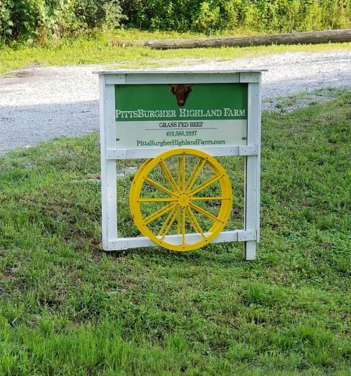 Sign for PittsBurgher Highland Farm, featuring a yellow wheel design, promoting grass-fed beef.