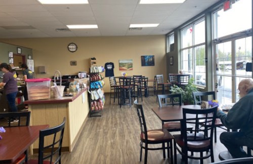 A cozy café interior with tables, a counter, and a customer enjoying a meal. Bright windows let in natural light.