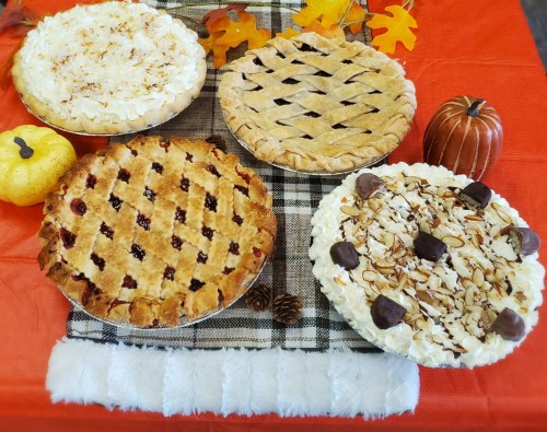Four delicious pies on a festive tablecloth: a cherry pie, a lattice apple pie, and two cream pies with toppings.