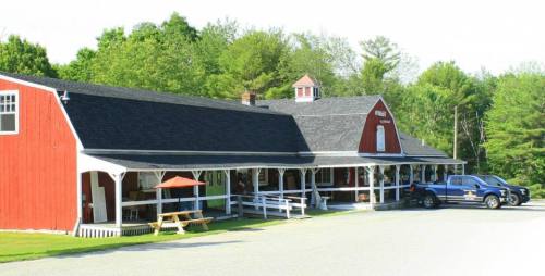 A red barn-style building with a porch, surrounded by greenery and parked vehicles in a rural setting.
