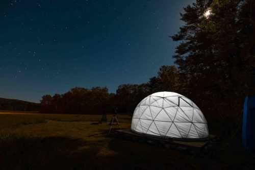 A geodesic dome under a starry night sky, surrounded by trees and a grassy field.