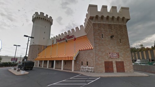 A castle-themed restaurant with a stone exterior, towers, and orange striped awnings, set in a parking lot.