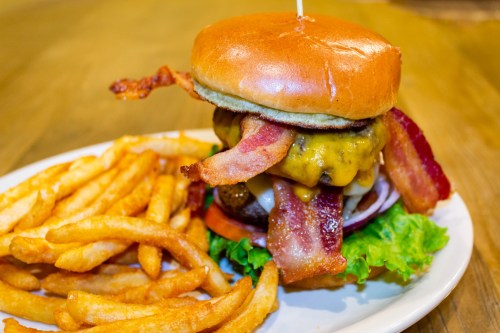 A juicy burger stacked with cheese, bacon, and fresh toppings, served with a side of crispy curly fries.