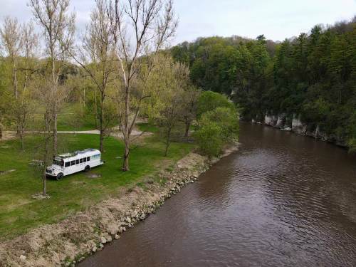A white bus parked by a river, surrounded by green trees and grassy areas. Scenic nature view.