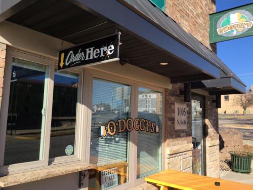 Exterior of a restaurant with a sign that says "Order Here" and "O'Doggy's" on the window. Bright, sunny day.
