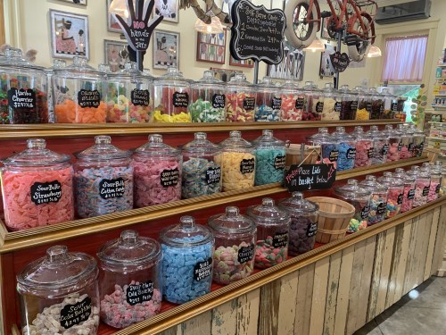 A colorful display of candy jars filled with various sweets on a wooden shelf in a charming shop.