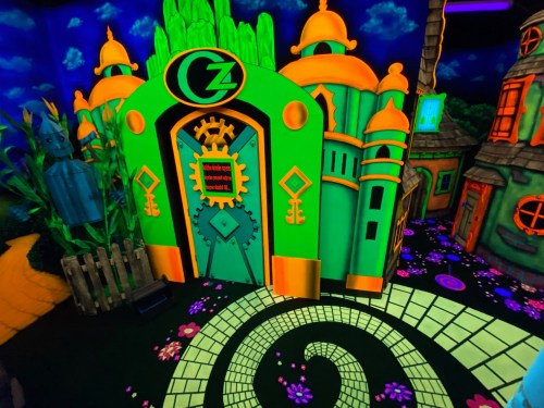 A vibrant, neon-colored building with whimsical architecture, surrounded by colorful plants and a spiraling path.