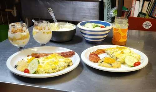 Two plates of breakfast with eggs, bacon, and vegetables, alongside parfaits and a bowl of salad.