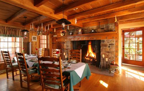 Cozy dining room with wooden beams, a stone fireplace, and a table set for a meal, surrounded by warm, inviting decor.