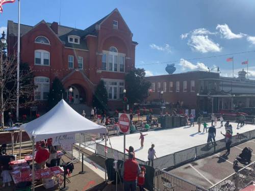 A festive outdoor ice skating rink in front of a historic building, with people skating and holiday decorations around.