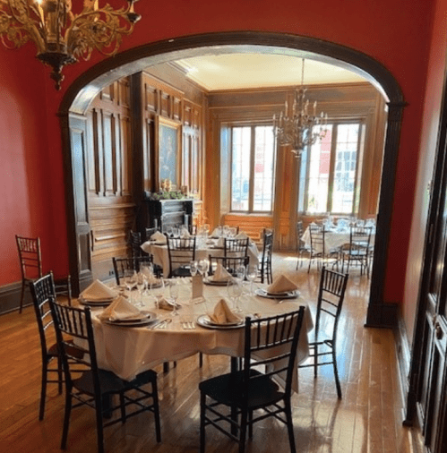 Elegant dining room with wooden accents, tables set with white linens, and large windows letting in natural light.