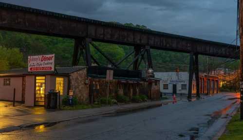 A diner beside a railway bridge, with wet streets reflecting the evening light and greenery in the background.