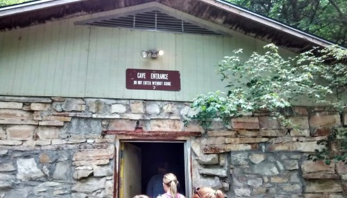 A group of people stands outside a stone building with a sign reading "Cave Entrance" above the door.