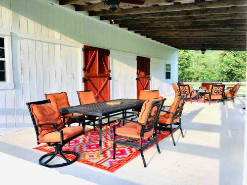 Outdoor patio with a dining table and chairs, featuring a colorful rug and wooden beams overhead.