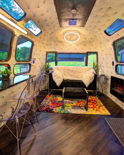 Cozy interior of a modern trailer with a plush sofa, colorful rug, and large windows, featuring stylish decor and plants.
