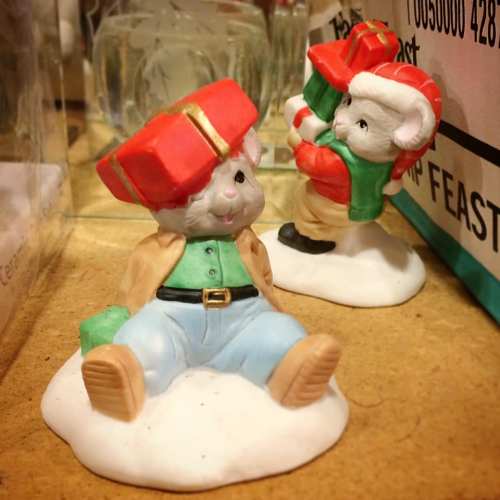 Two cute figurines: one sitting on snow, wearing a red hat and green outfit, and another standing with a gift.