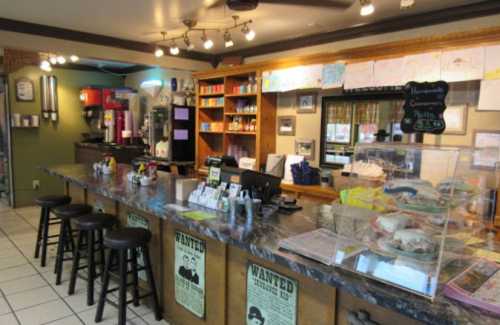 A cozy café interior featuring a marble counter, stools, and a display case with pastries. Colorful artwork decorates the walls.