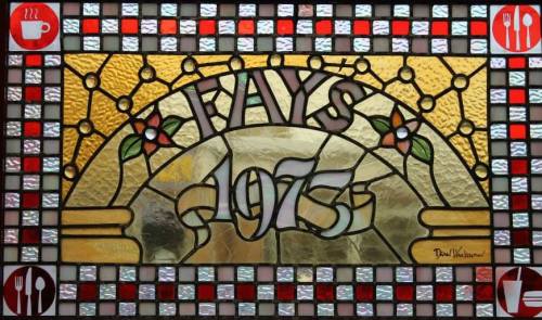Stained glass window featuring "Fay's 1973" with decorative flowers and icons of cups and utensils.