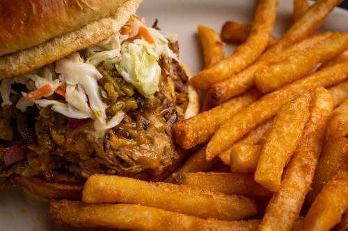 A close-up of a pulled pork sandwich topped with coleslaw, served with a side of golden, crispy French fries.