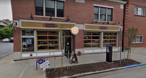 A brick building with large windows, featuring a restaurant entrance and outdoor signage, set on a city street.