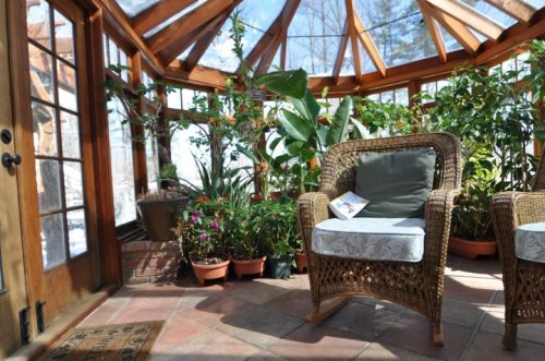 A sunlit greenhouse with wooden beams, potted plants, and wicker chairs, creating a cozy, inviting atmosphere.