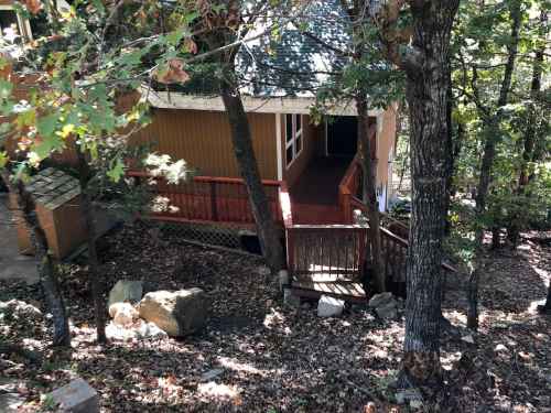 A wooden cabin nestled among trees, with a deck and stone pathway, surrounded by fallen leaves.