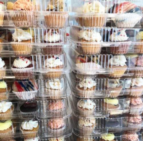 A display of colorful cupcakes stacked in clear plastic containers, showcasing various frosting and toppings.