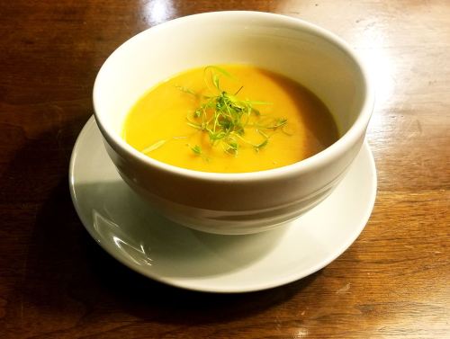 A bowl of creamy orange soup garnished with fresh herbs, placed on a white saucer against a wooden table.