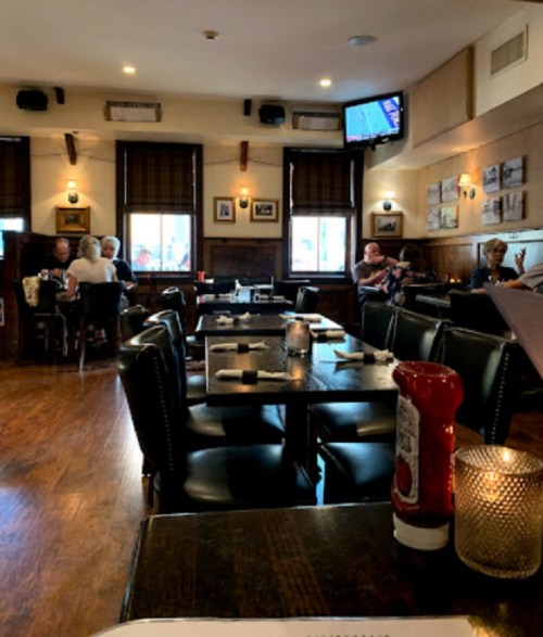 A cozy restaurant interior with wooden floors, tables set for dining, and patrons enjoying their meals.