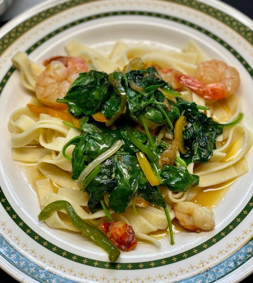 A plate of fettuccine topped with shrimp, sautéed spinach, and colorful bell peppers in a light sauce.