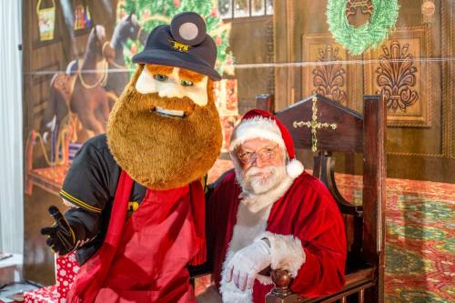 A person in a bear costume and Santa Claus pose together in a festive setting with holiday decorations.