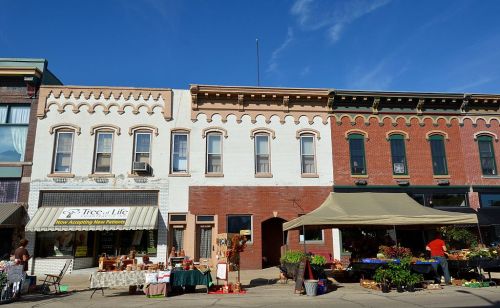 A charming street scene featuring historic buildings and a market with flowers and goods for sale under a canopy.