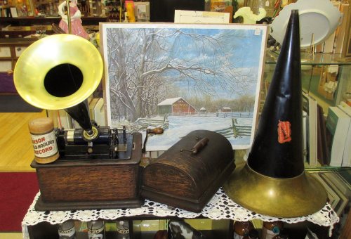 A vintage display featuring a gramophone, a wooden box, and a large horn, with a winter landscape painting in the background.