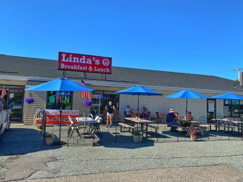 Outdoor seating area at Linda's Breakfast & Lunch, with patrons enjoying meals under blue umbrellas on a sunny day.