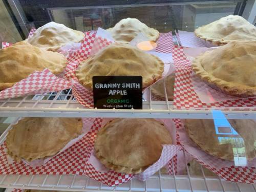 A display of freshly baked Granny Smith apple pies in a bakery case, labeled as organic from Washington State.